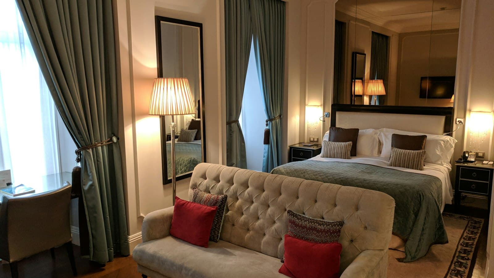 A guest room with a tufted sofa, draped windows, and a mirrored wall